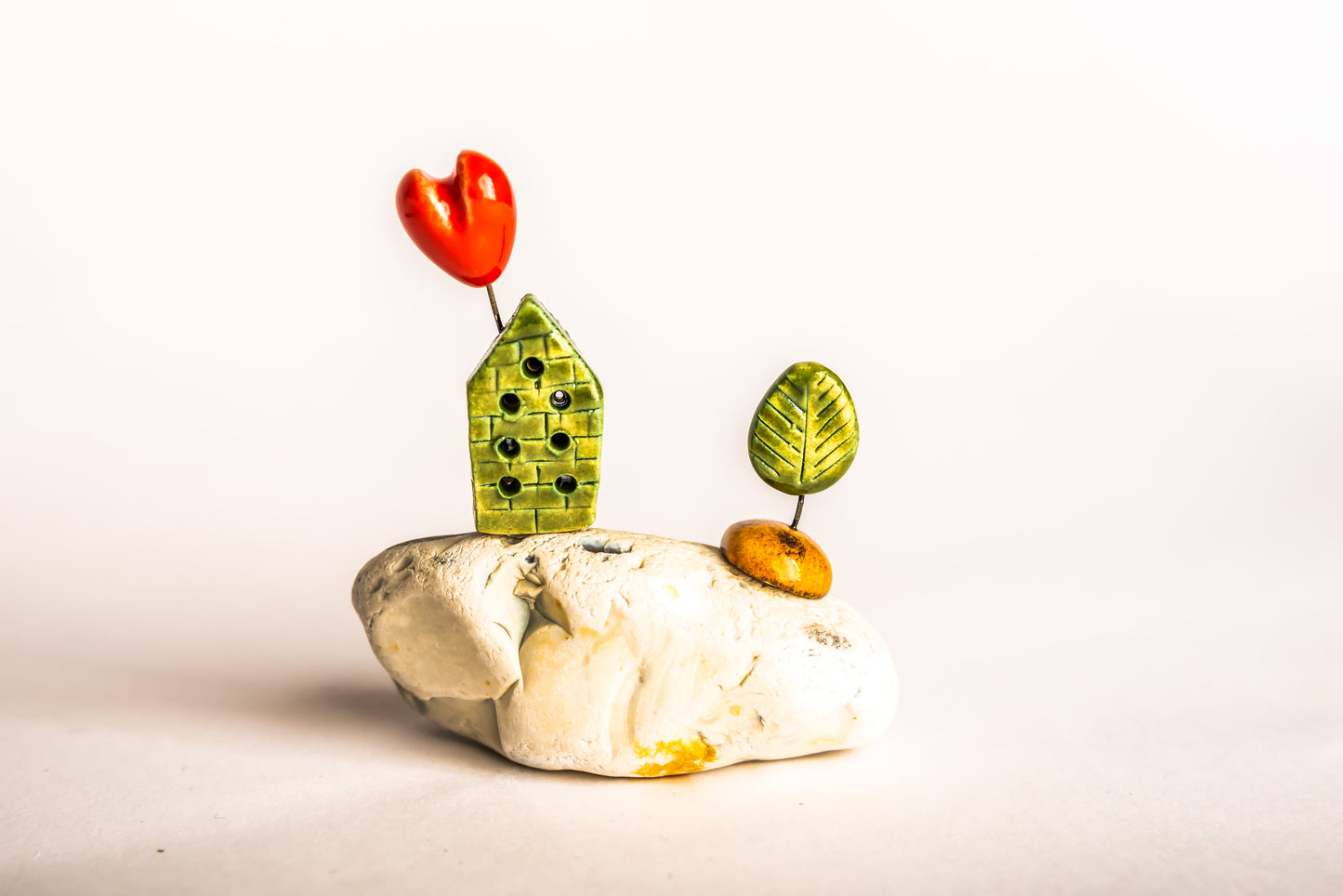 Hand-built green ceramic house on a rock, with a tree