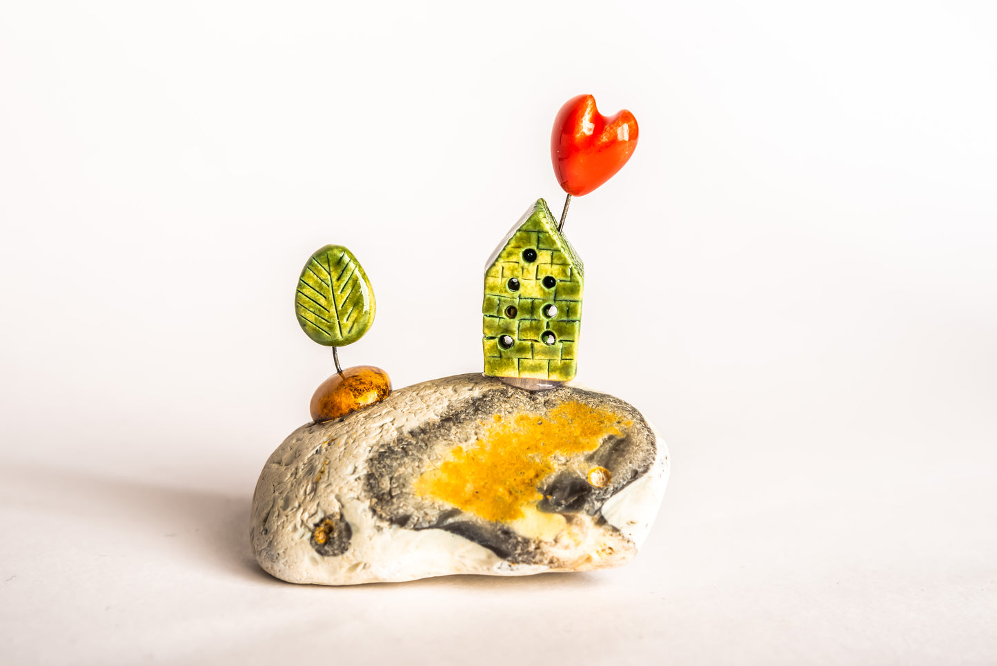 Hand-built green ceramic house on a rock, with a tree