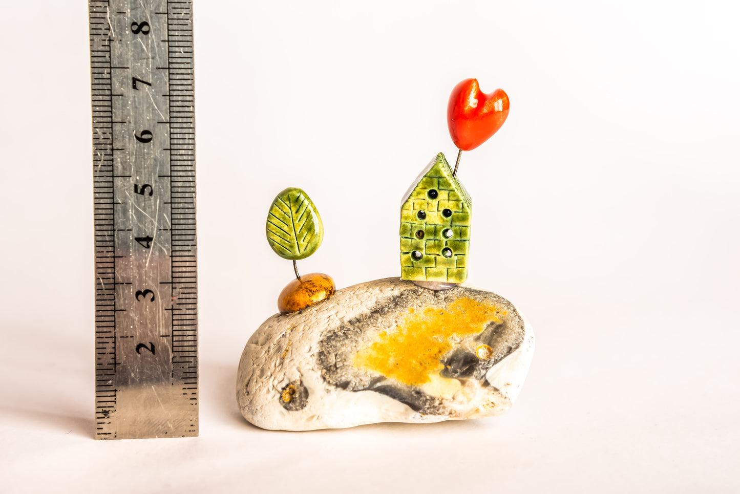 Hand-built green ceramic house on a rock, with a tree
