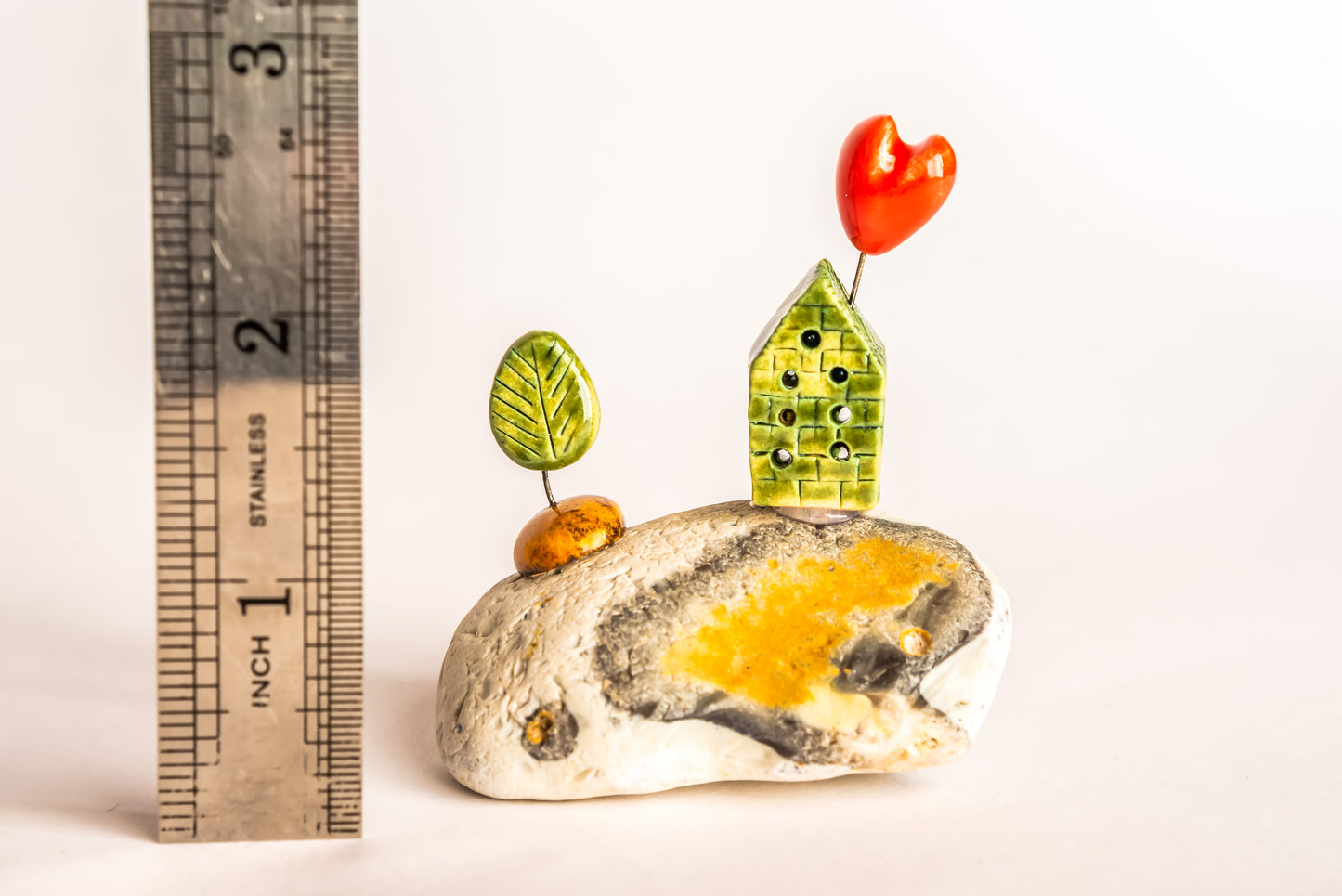 Hand-built green ceramic house on a rock, with a tree